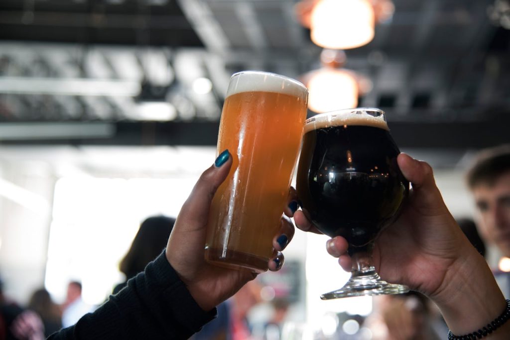 selective-focus-photography-of-people-having-a-toast-1269043 Two hands clink glasses of different craft beers, capturing a celebratory moment in a modern bar.